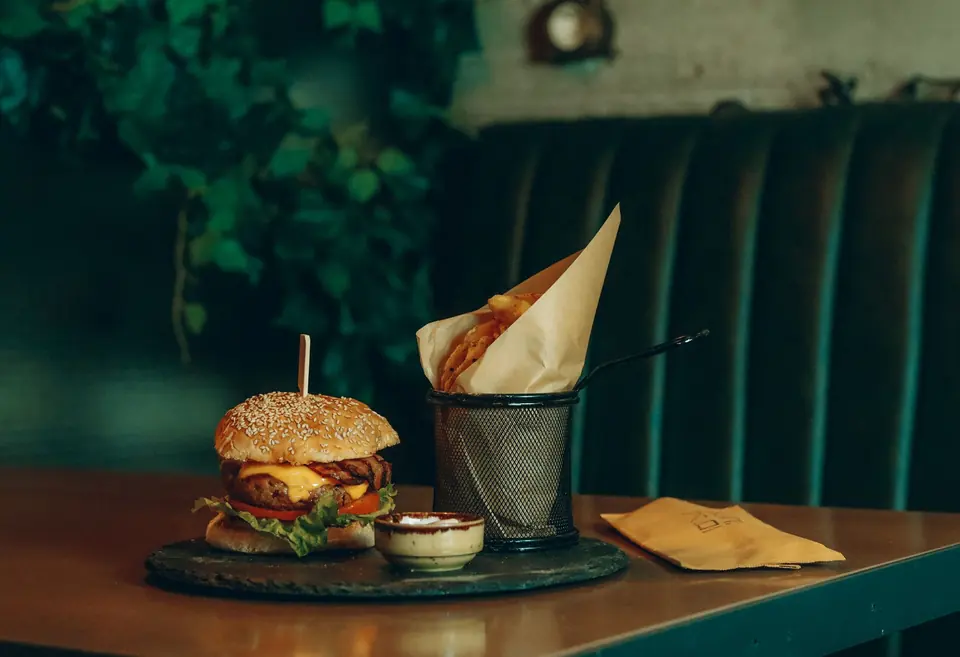 Cheeseburger and fries in a paper cone on a table in a green-boothed restaurant